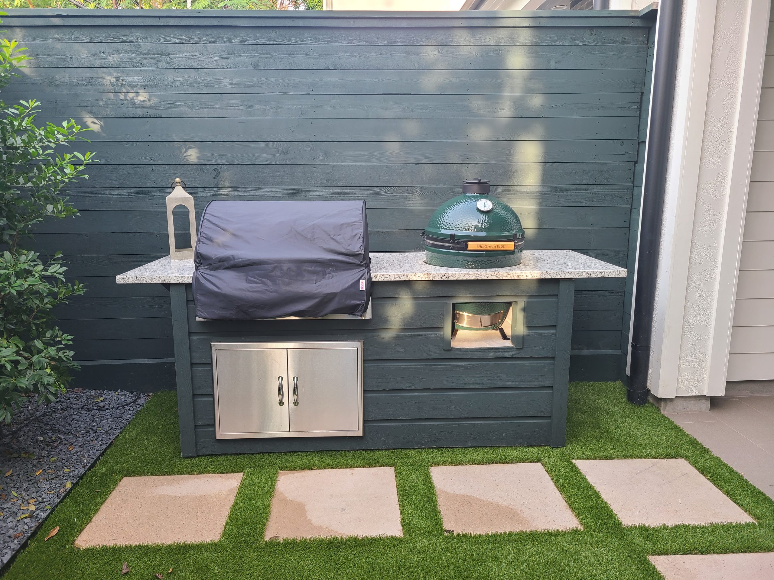 Custom outdoor bbq island installed with synthetic grass accents and pavers.