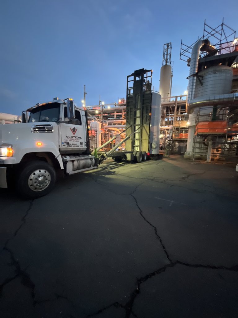 Semi-truck transporting large cone-bottom polyethylene tanks for industrial site delivery